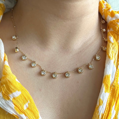 Necklace with small diamonds worn by a person in a yellow and white patterned top.