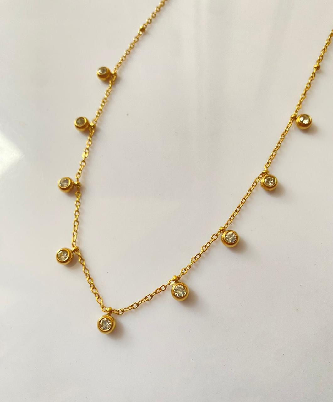 Gold necklace with small round pendants on a light background