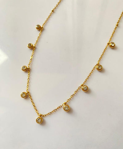 Gold necklace with small round pendants on a light background